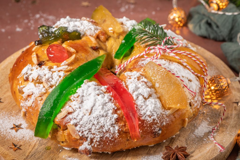 Ein portugiesischer Weihnachtskuchen Bolo Rei liegt mit Puderzucker und kandierten Früchten auf einem Brett.