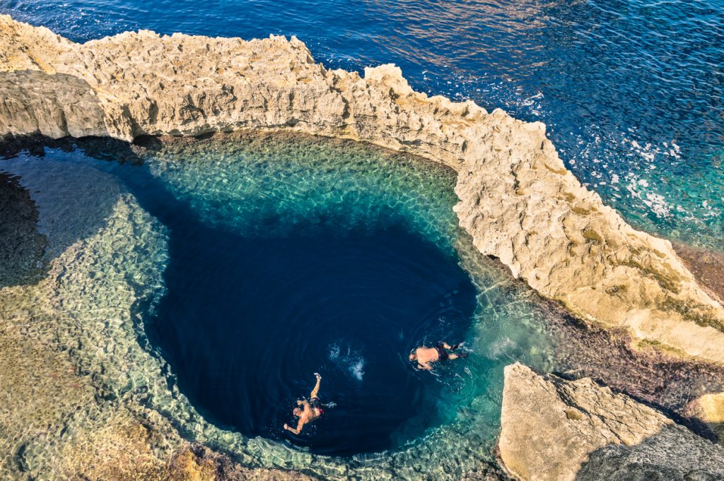 Zwei Schnorchler ziehen ihre Bahnen im kreisrunden, tiefblauen Blue Hole an der Felsenküste von Malta.