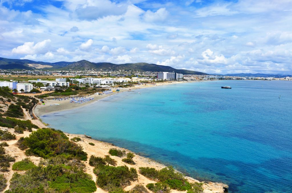 Panorama über die Playa d’en Bossa mit flachem, blauem Wasser, Strandabschnitt und Hotelanlagen an der Küstenlinie.