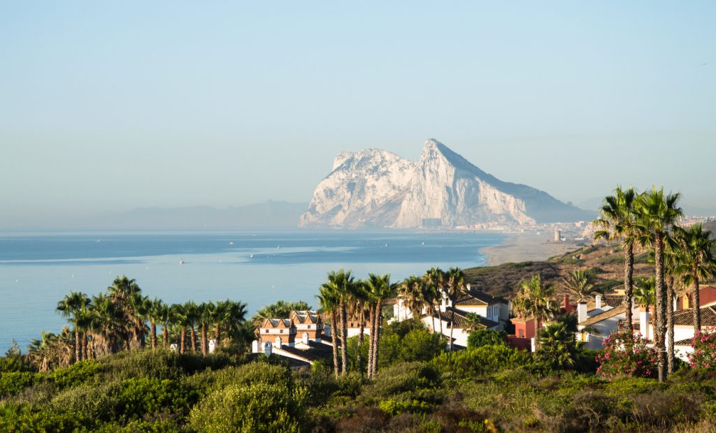 Küstenlandschaft mit Palmen und Ferienhäusern in Spanien und der Felsen von Gibraltar am Horizont.