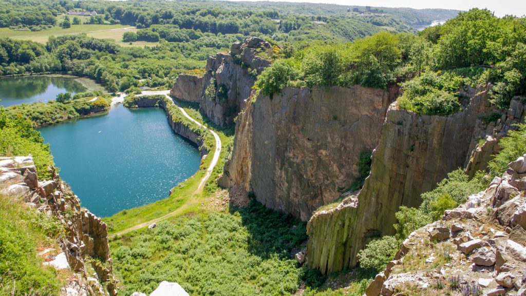 Steile Klippen und ein türkisblauer See in einem ehemaligen Steinbruch auf Bornholm.