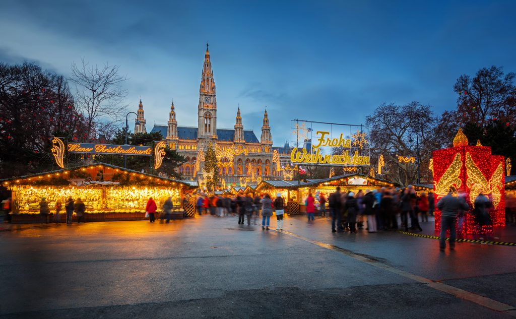 Abendaufnahme des Christkindlmarkts vor dem Rathaus in Wien mit vielen Lichtern und Besuchern.