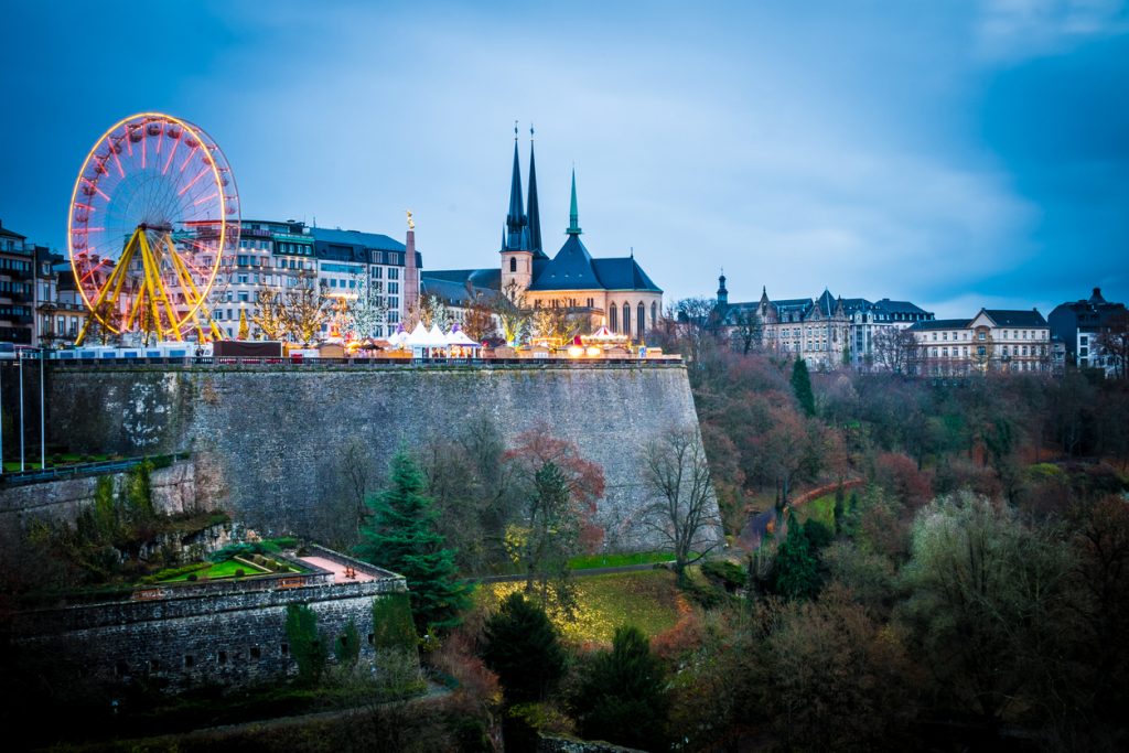 Dämmerungsblick auf Luxemburg Stadt mit Riesenrad, Lichterketten und Silhouette der Altstadt.