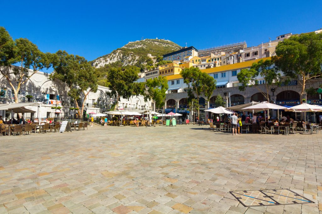 Sonniger Platz in Gibraltar mit Cafés, Sonnenschirmen und Häusern am Hang.