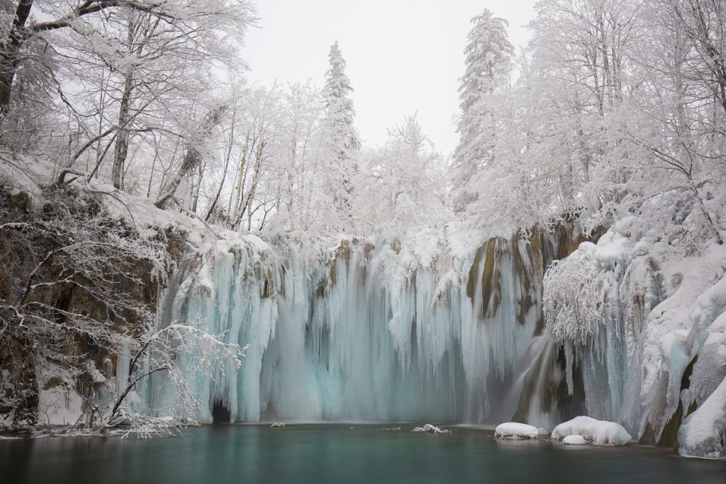 Ein vereister Wasserfall hängt im Winter im Nationalpark Plitvicer Seen über einem türkisfarbenen Becken.