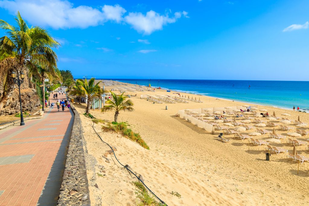 Promenade neben einem breiten Sandstrand mit Liegen und Sonnenschirmen auf Fuerteventura.