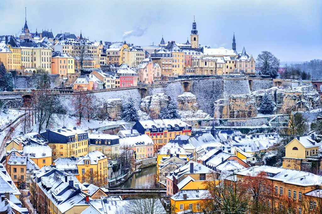 Verschneite Altstadt von Luxemburg Stadt mit bunten Häusern, Felsen und Festungsmauern.