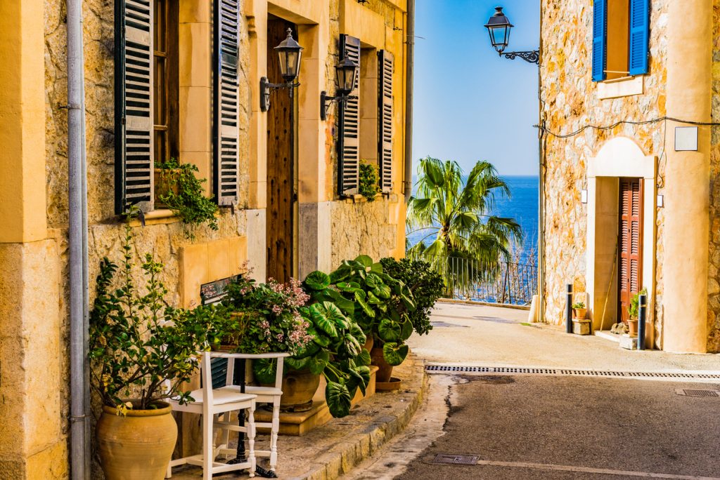 Schmale Gasse mit Steinmauern, vielen Pflanzen und Meerblick im Dorf Banyalbufar.