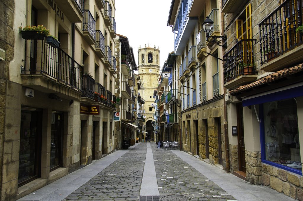 Eine schmale Altstadtstraße in Bilbao mit Balkonen und Kirchturm.