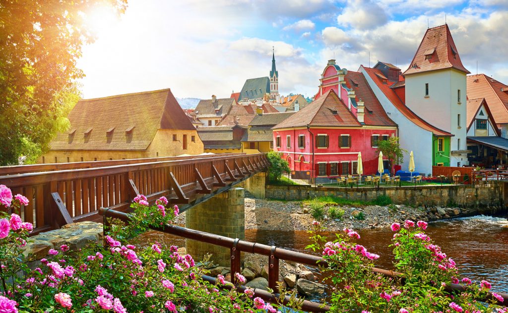 Historische Altstadt mit Holzbrücke, bunten Häusern und Kirchturm am Fluss in Tschechien.