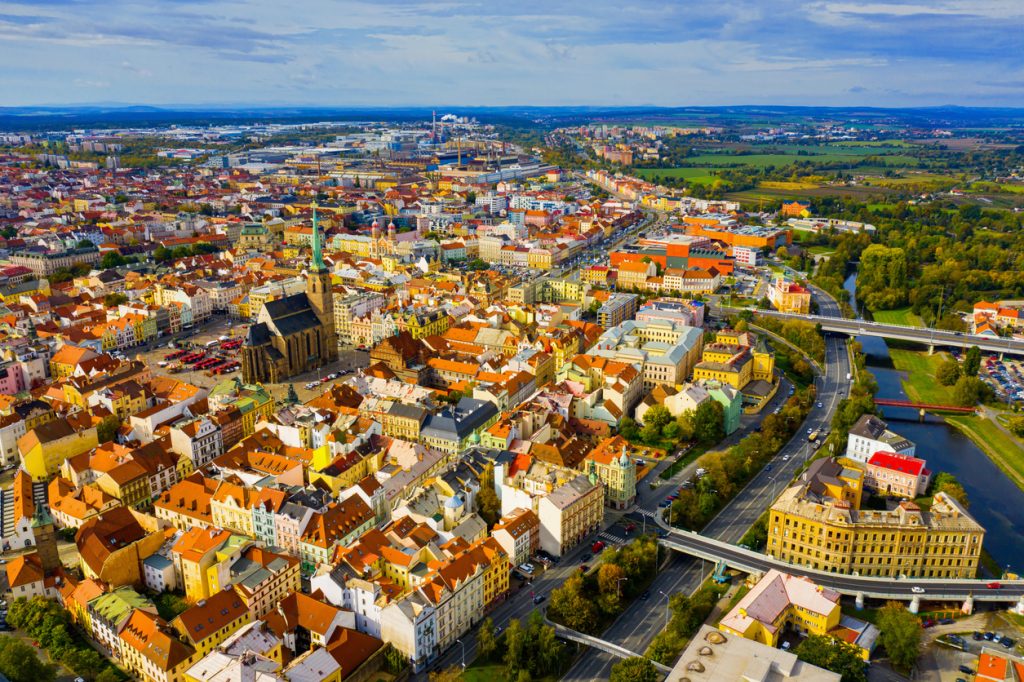 Luftaufnahme von Pilsen mit dicht bebauter Altstadt, Kirchturm und Fluss neben breiten Straßen.