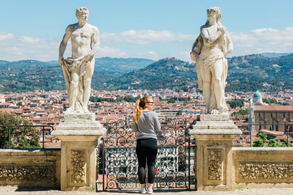 Eine Person steht an einem Aussichtspunkt in Florenz zwischen zwei großen Statuen und blickt über die Stadt.