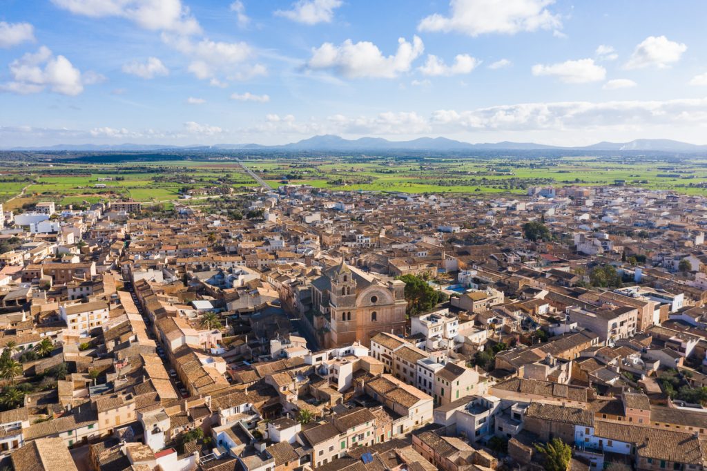Weitwinkel-Luftaufnahme von Campos auf Mallorca mit dichtem Ortskern, Feldern und Bergen in der Ferne.