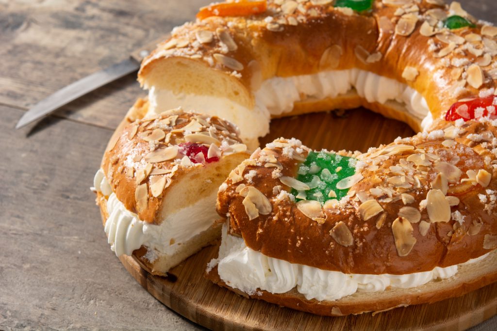 Ein Stück Roscón de Reyes ist angeschnitten und zeigt eine dicke Schicht Sahnefüllung zwischen den Teigringen.