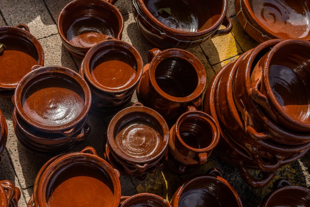 Verschiedene braun glasierte Keramiktöpfe und Schüsseln stehen dicht nebeneinander auf Pflastersteinen.