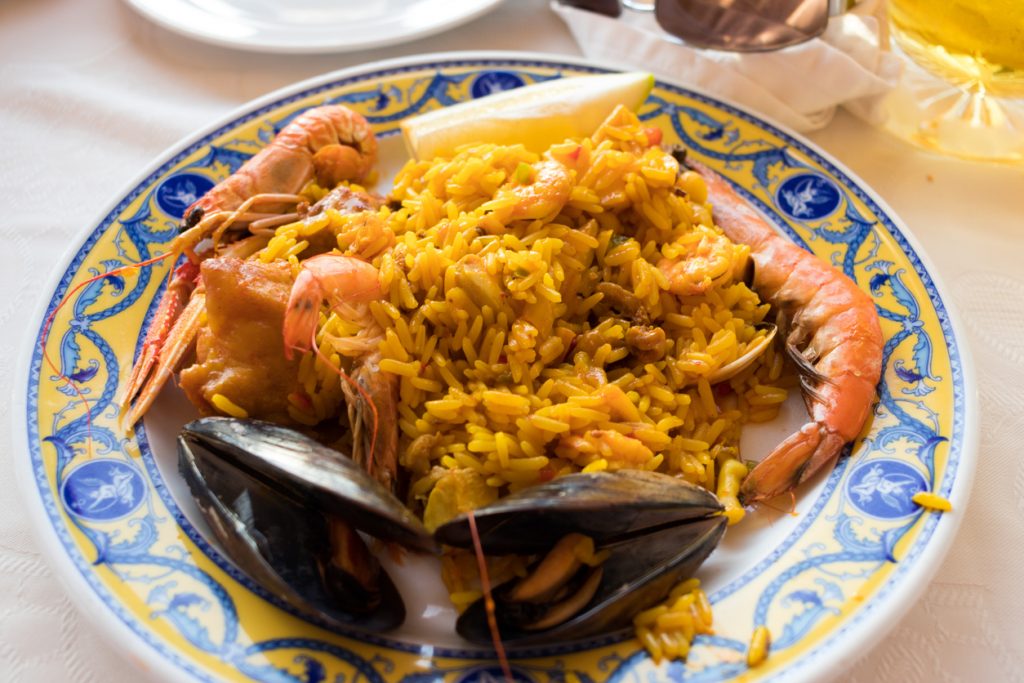 Ein Teller Paella wird mit Garnelen und Muscheln auf einem bunten Randteller serviert.