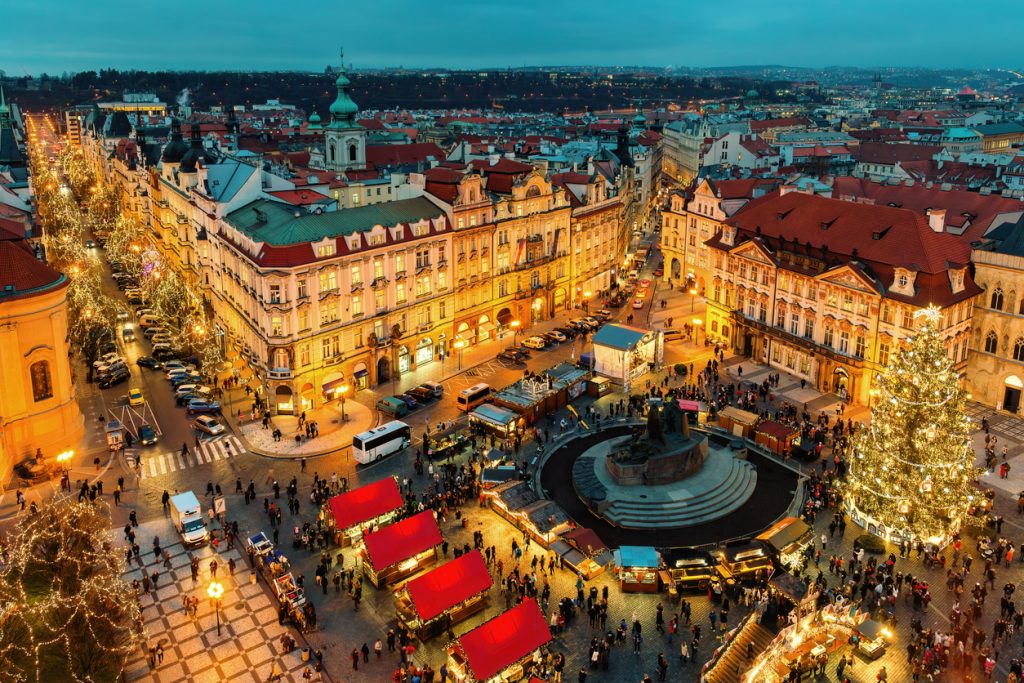 Festlich beleuchteter Platz in Prag mit Marktständen, Weihnachtsbaum und vielen Menschen am Abend.