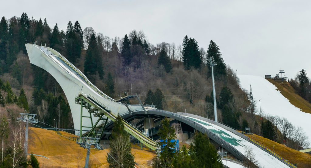 Die Skisprungschanze in Garmisch-Partenkirchen steht am Hang vor Wald und grauem Himmel.