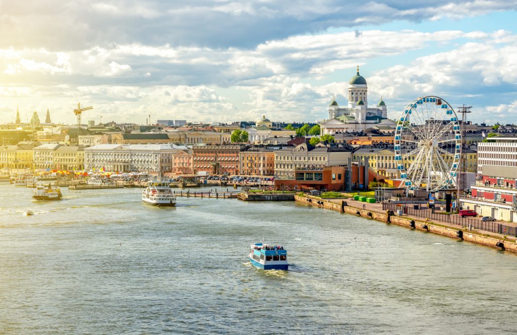Boote fahren im Hafen von Helsinki, während das Riesenrad und die Skyline im Hintergrund liegen.
