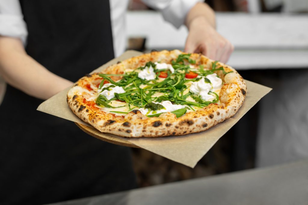 Eine Pizza mit Rucola und cremigem Belag wird auf einem Brett in Florenz serviert.