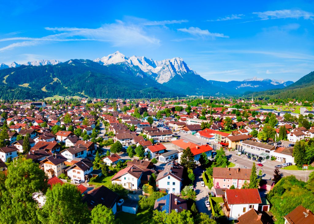 Weitblick über Garmisch-Partenkirchen mit roten Dächern und schneebedeckten Gipfeln am Horizont.