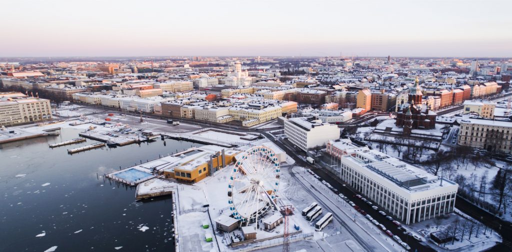 Der Hafenbereich von Helsinki liegt im Schnee, mit Riesenrad, Uferstraße und vereistem Wasser.