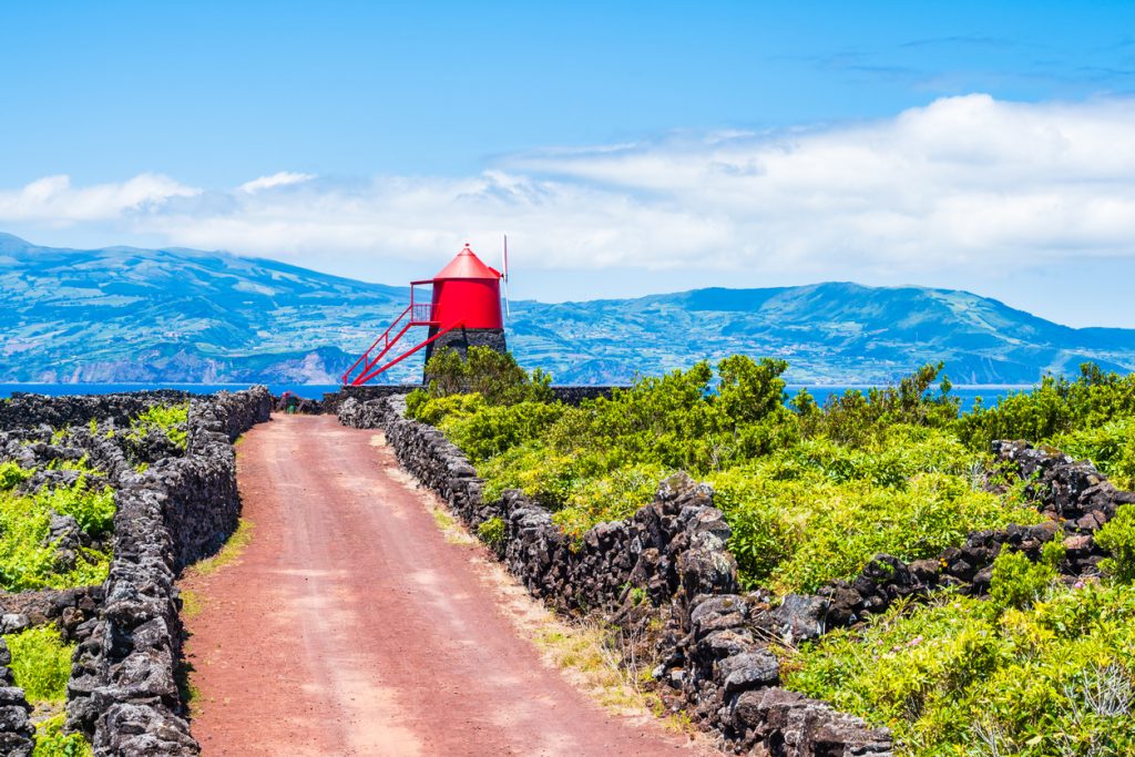 Roter Leuchtturm an einem Weg zwischen Steinmauern auf den Azoren.