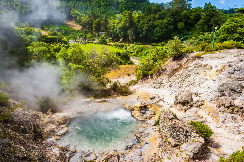 Thermalquelle mit aufsteigendem Dampf in einer grünen Landschaft auf den Azoren.