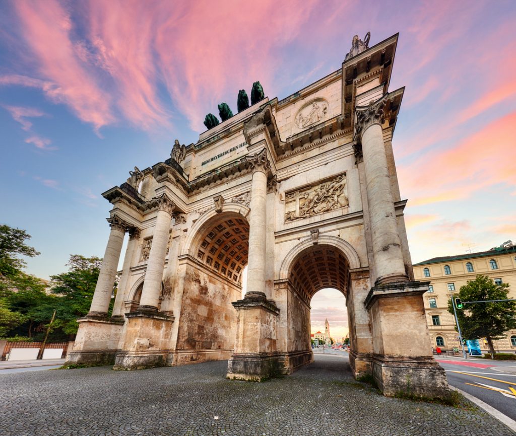 Das Siegestor in München steht vor einem rosa Himmel und wirkt im Weitwinkel besonders monumental.