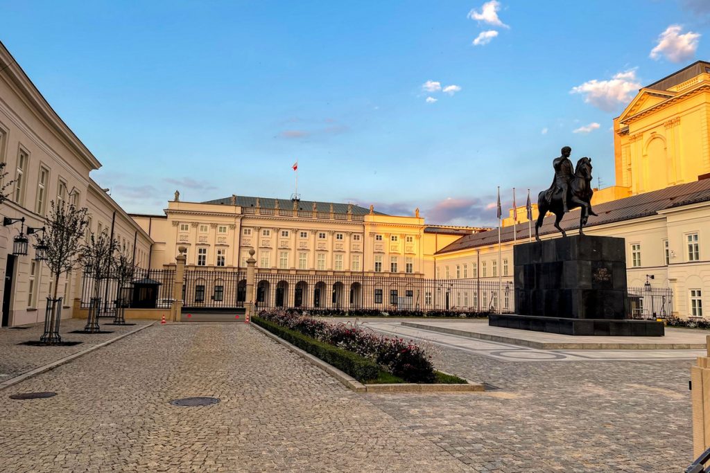 Ein Reiterdenkmal steht vor einem hellen Palais in Warschau im sanften Abendlicht.