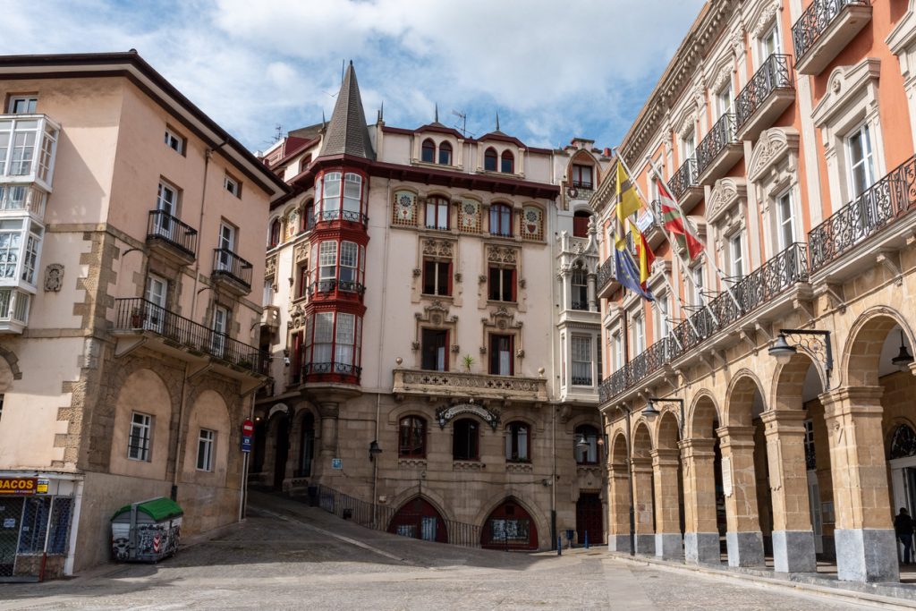 Der Rathausplatz in Bilbao mit Arkaden, Flaggen und historischer Architektur.
