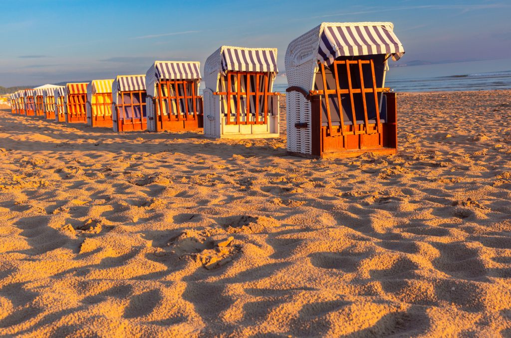 Eine Reihe von Strandkörben steht auf goldenem Sand nahe der Wasserlinie.
