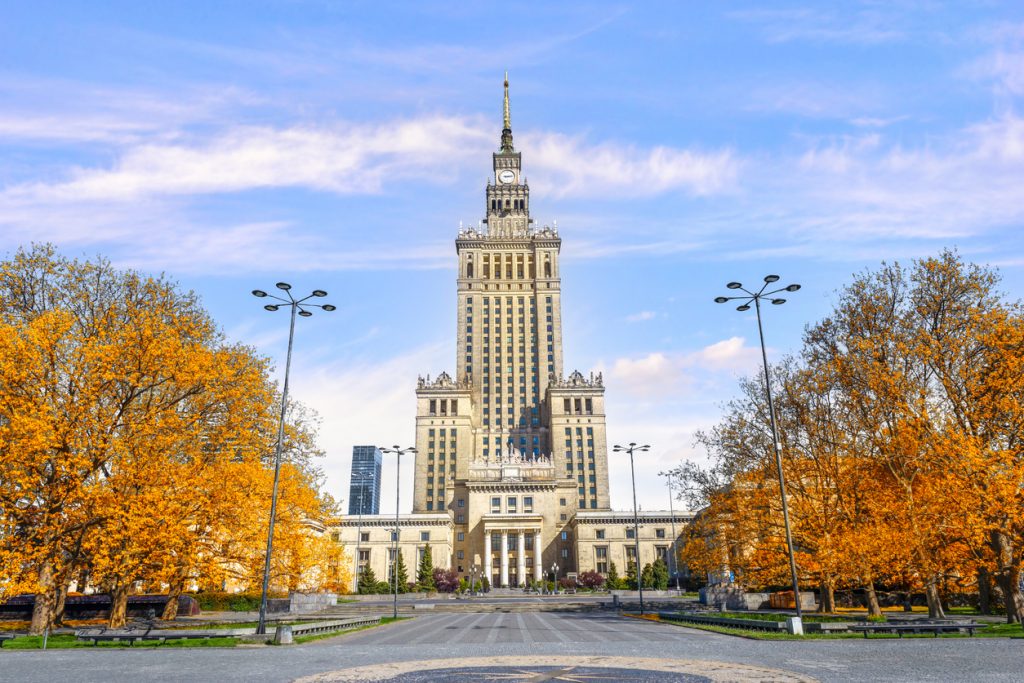 Der Kulturpalast in Warschau steht zentral zwischen herbstlichen Bäumen und breiten Wegen.
