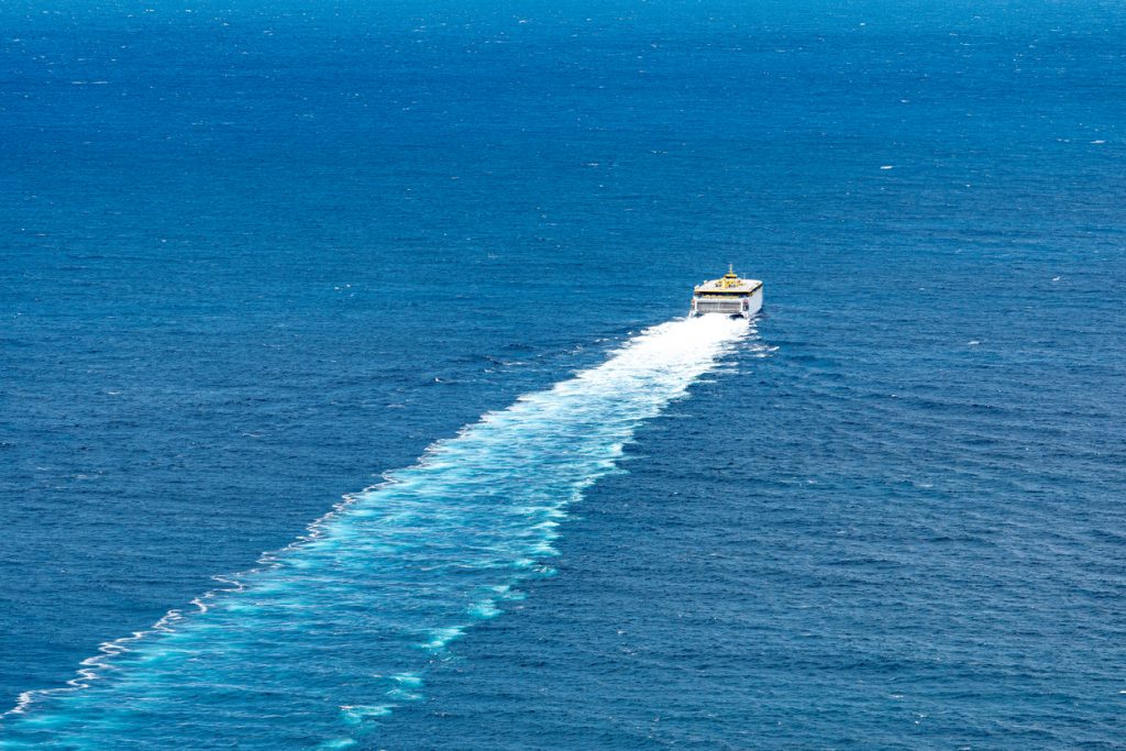 Eine Fähre fährt über das offene Meer und zieht eine lange, helle Bugwelle hinter sich her.