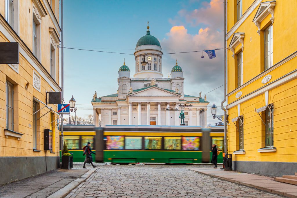 Eine grüne Straßenbahn fährt in Helsinki durch eine Straße, im Hintergrund steht der weiße Dom.