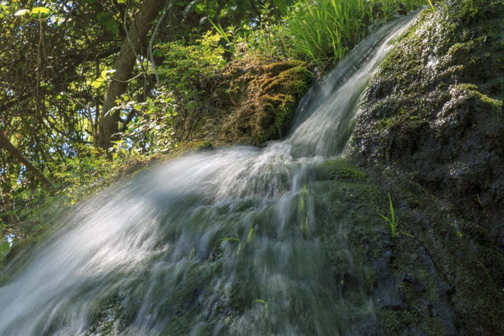 Kleiner Wasserfall am Salt des Freu auf Mallorca, der über moosige Steine fließt.