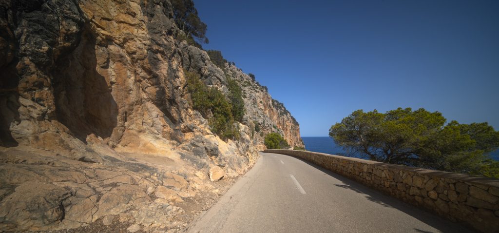 Schmale Straße bei Capdepera entlang einer Felswand über dem Meer.