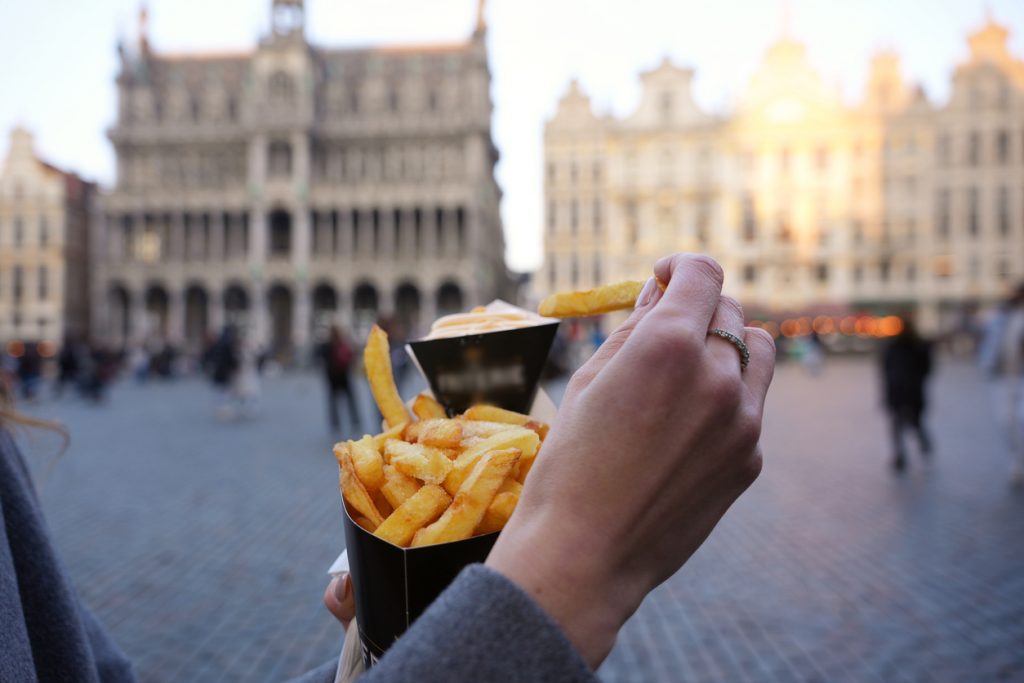Hand hält eine Portion Pommes auf einem Platz in Brüssel.