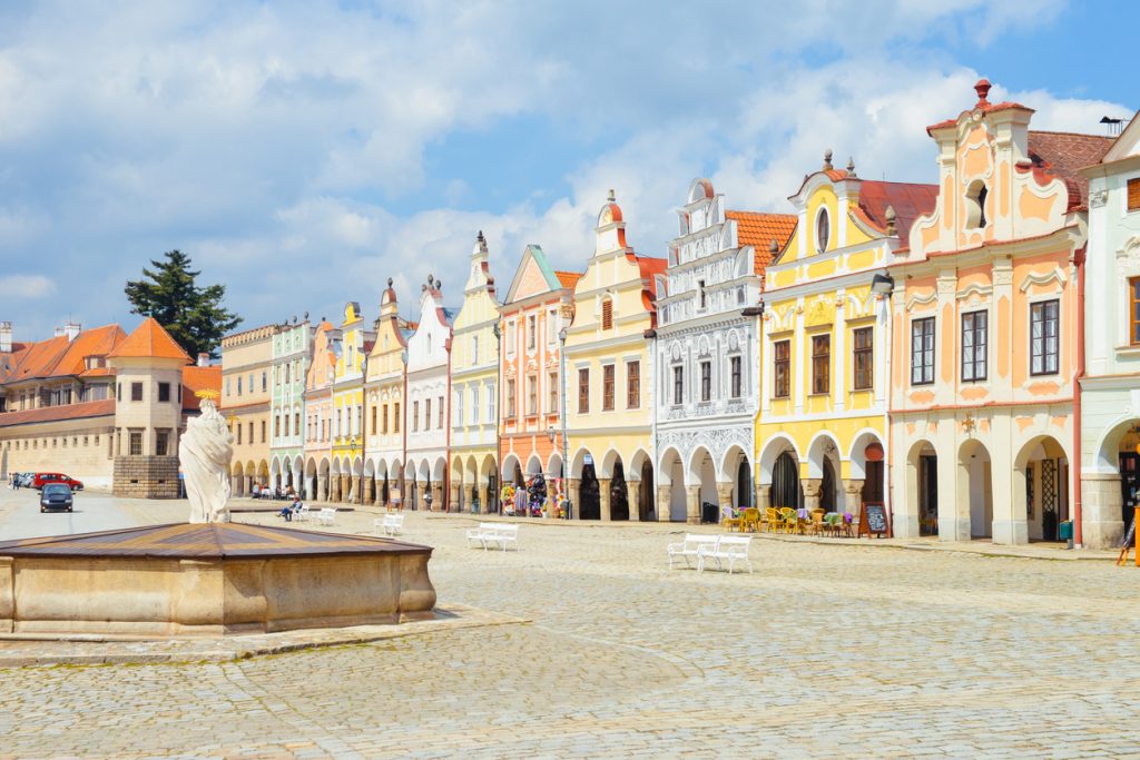 Bunte Renaissance- und Barockfassaden mit Arkaden am großen Platz in Telč bei hellem Tageslicht.