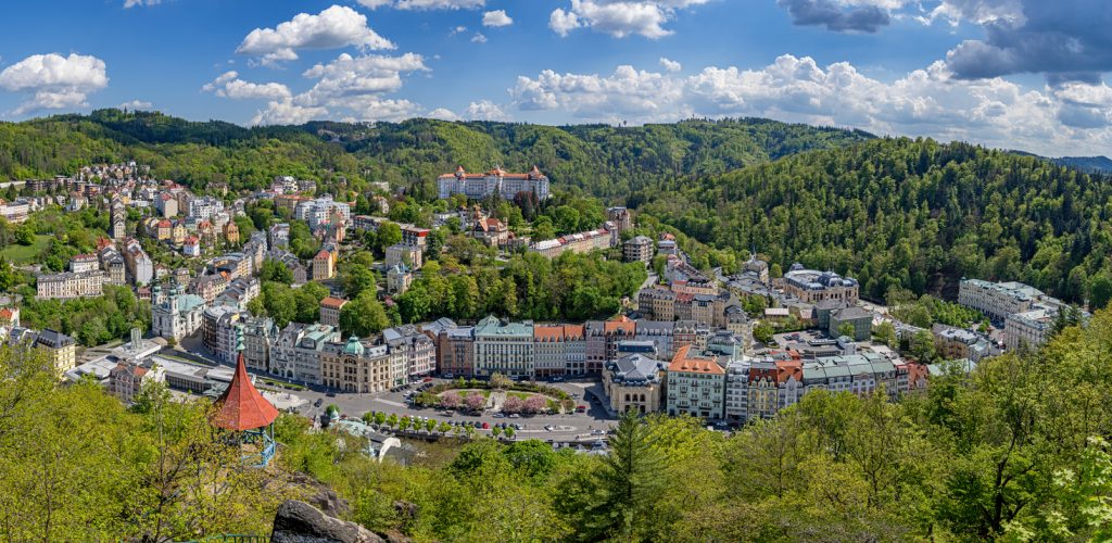 Weitblick über Karlsbad mit Kurviertel, grünen Wäldern und Hügeln unter wolkigem Himmel.