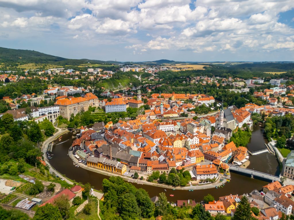 Luftaufnahme einer Altstadt in einer Flussschleife mit roten Dächern und Brücken in Tschechien.