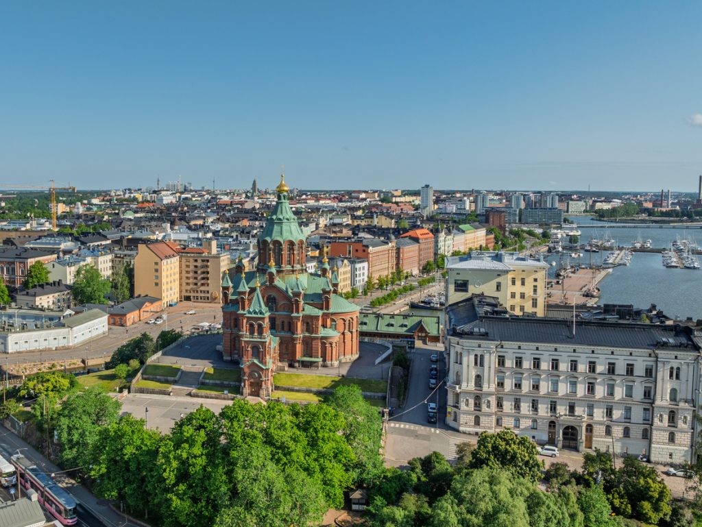Eine Luftaufnahme von Helsinki zeigt die rote Kathedrale, grüne Ufer und den Hafen mit Booten.