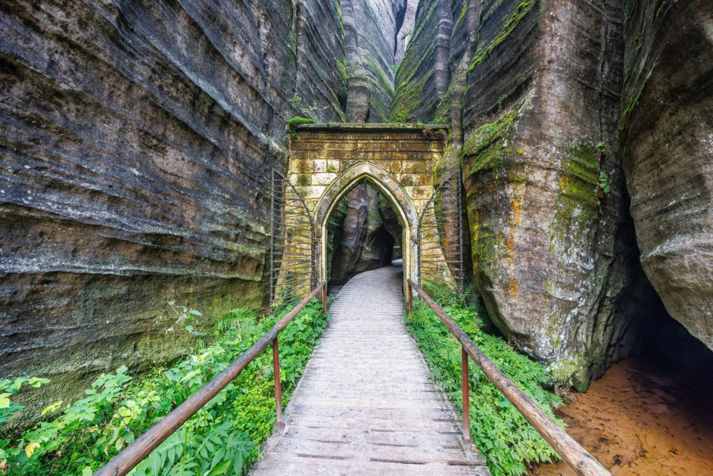 Holzsteg führt durch eine enge Sandsteinschlucht zu einem steinernen Torbogen.
