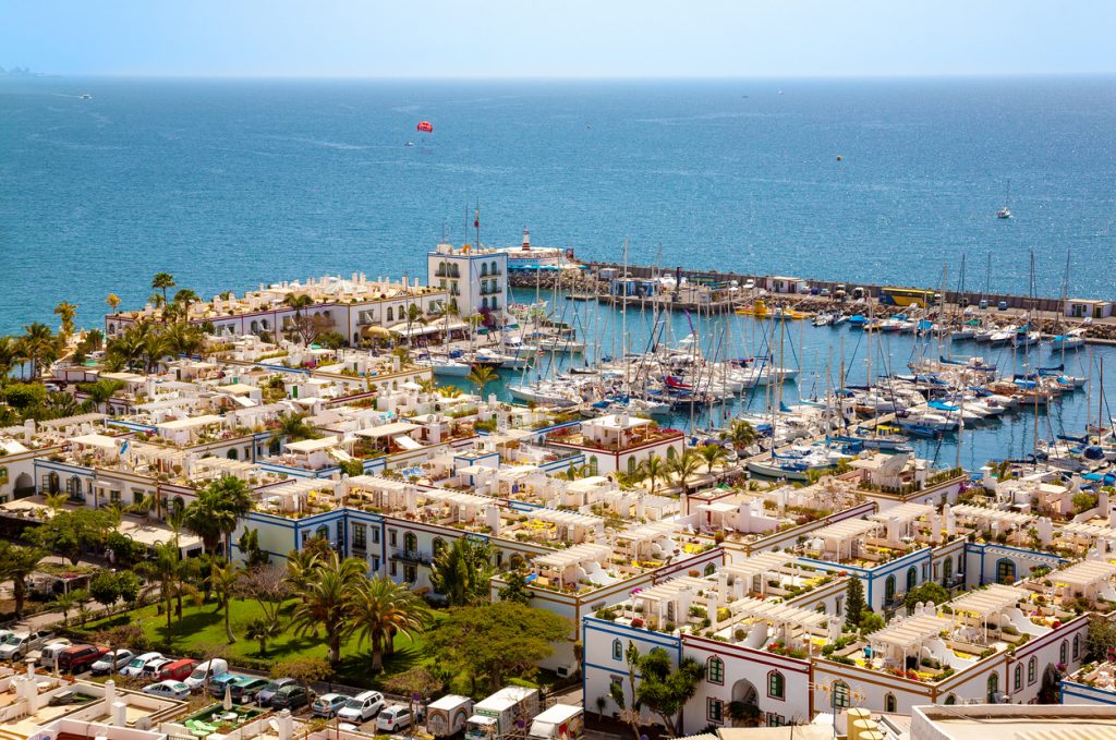 Ein Hafenbecken ist voller Segelboote vor weißen Häusern am Meer.