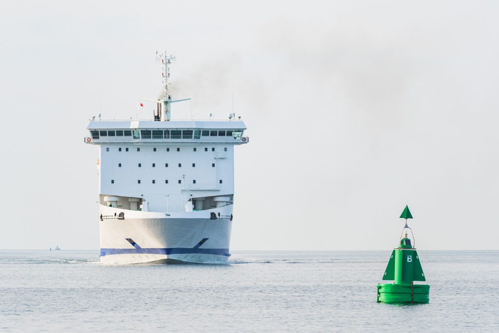 Eine große weiße Fähre fährt auf ruhigem Wasser an einer grünen Boje vorbei.