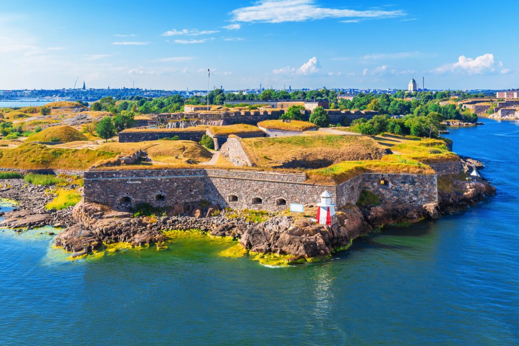 Eine Küstenfestung bei Helsinki liegt auf Felsen im Meer, vorne steht ein kleiner Leuchtturm.