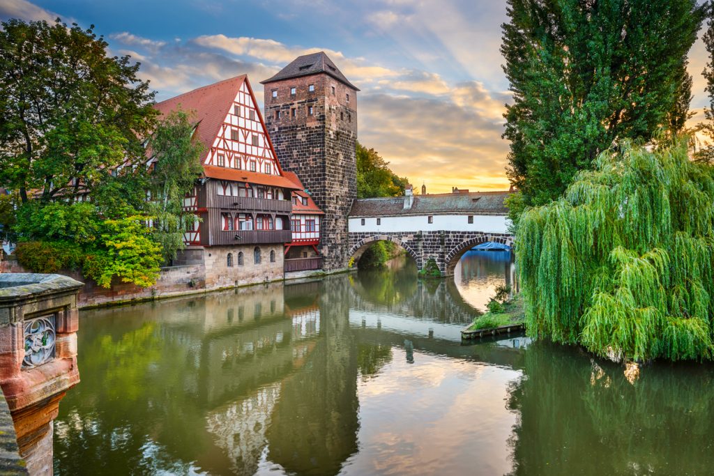 Fachwerkhaus und Brückenbogen spiegeln sich in der Pegnitz vor warmem Abendhimmel in Nürnberg.