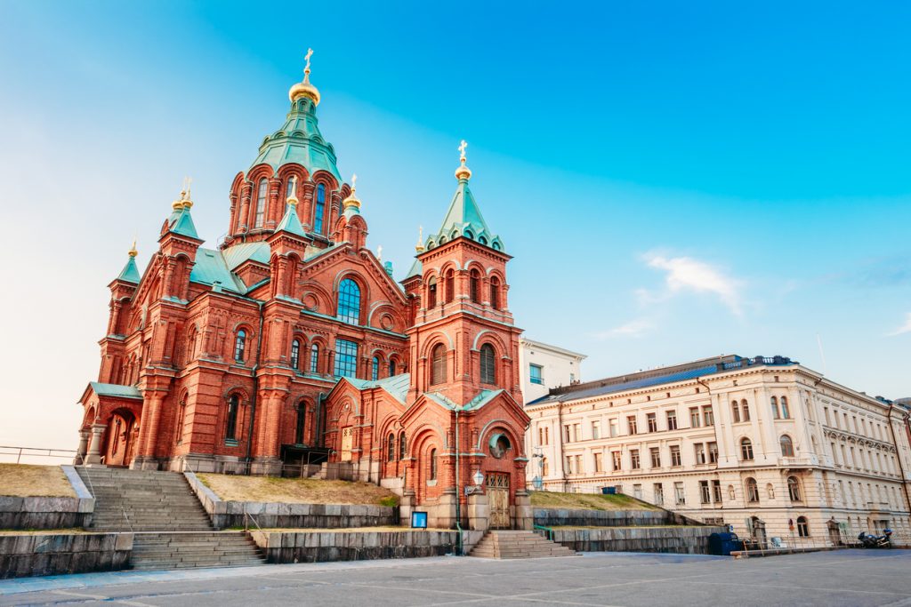 Eine rote Backstein-Kathedrale in Helsinki steht vor hellem Himmel und schneebedecktem Boden.