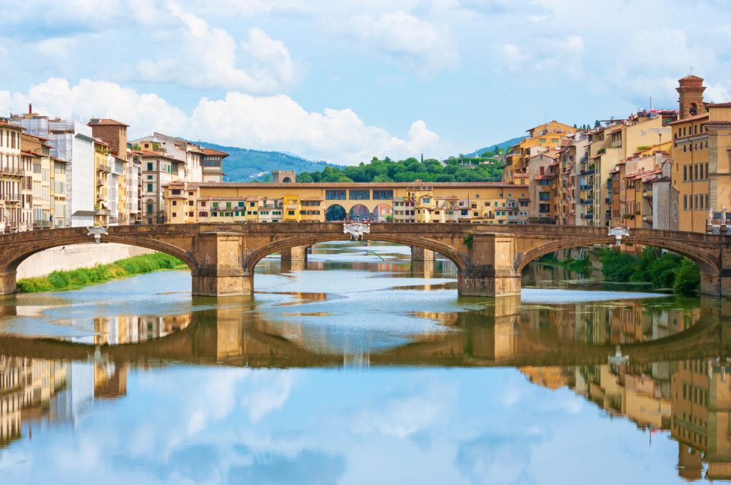 Eine Steinbrücke spannt sich über den Arno und spiegelt sich im Wasser in Florenz.