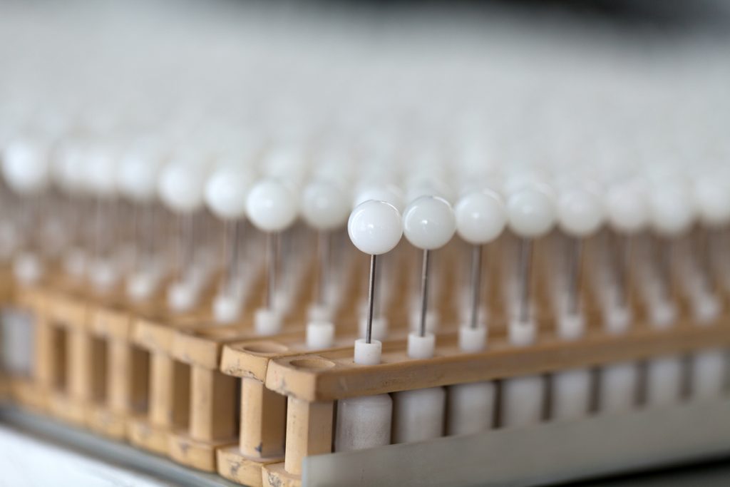 Weiße Perlenrohlinge stecken auf dünnen Metallstiften in einer Halterung und verschwimmen nach hinten im Bokeh.